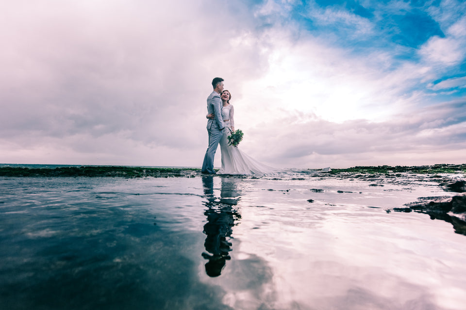 A couple who are in their wedding dress standing on a beach as the photographer takes their picture - Tim Downer Celebrant